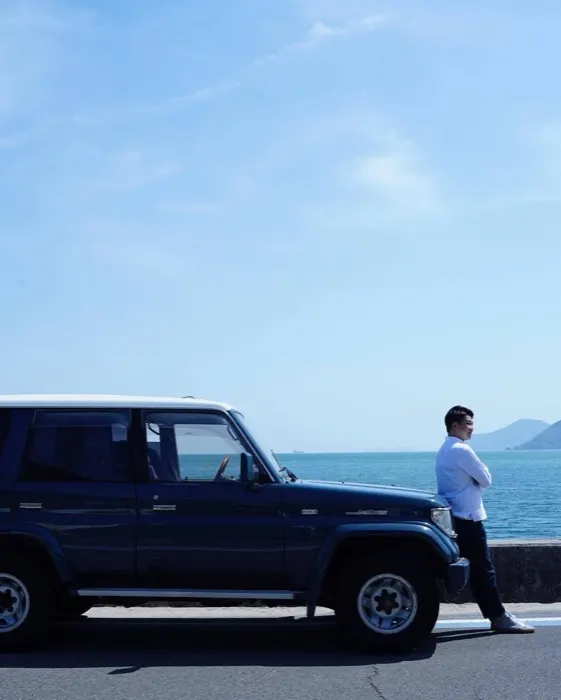 海沿いに停めた車の前に立つ髙田勇太